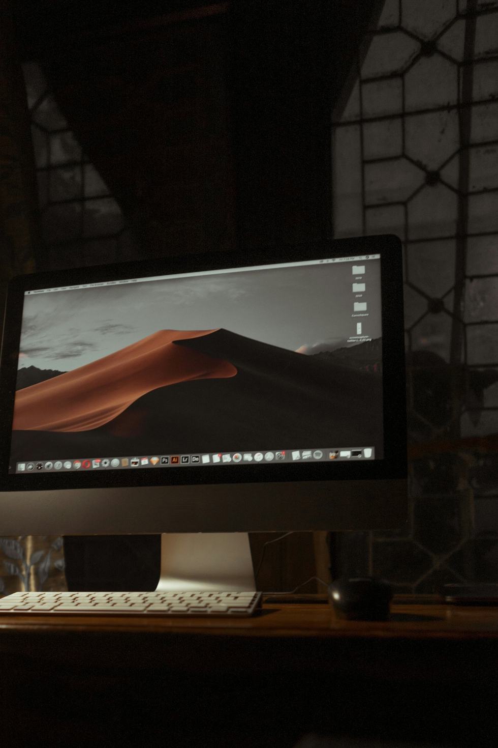 Werkplek bij avond: een beeldscherm en toetsenbord op een houten bureau in een donkere ruimte